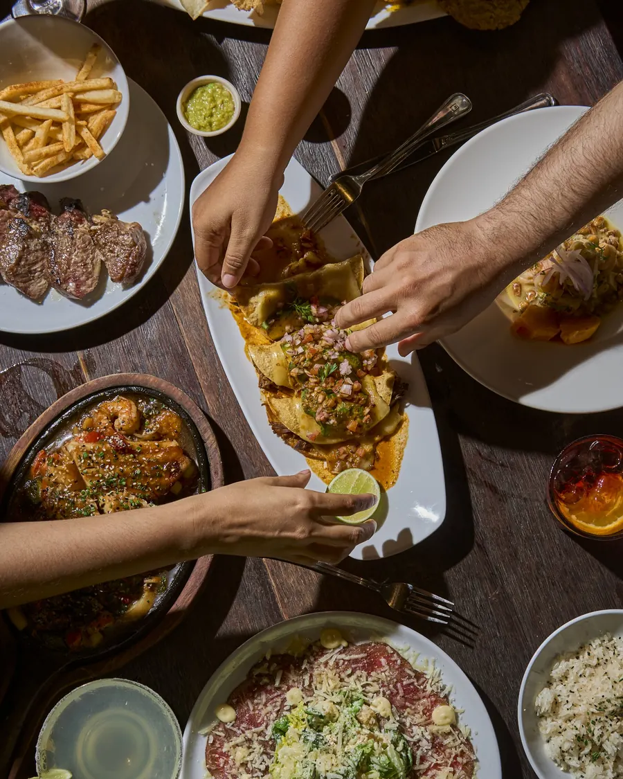 Friends sharing enchiladas, carpaccio and fried seafood at a Tentadero table